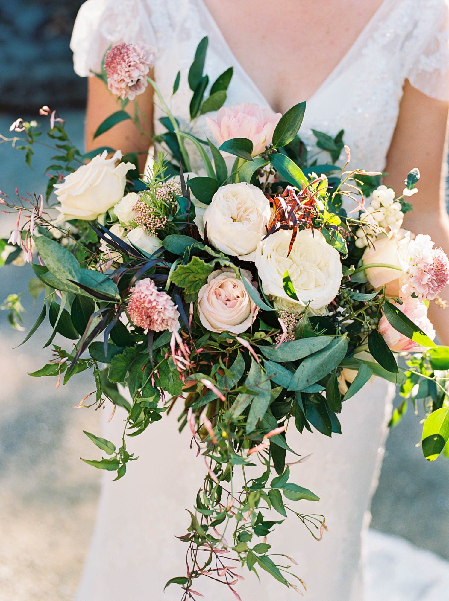  Closeup of bride holding cascading bouquet of white and blush pink garden roses, greenery and jasmine 