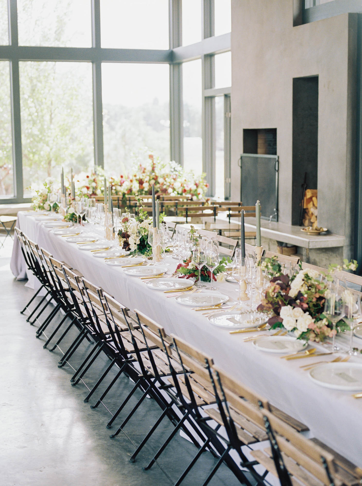  Long wedding dinner table with light gray tablecloth, bistro chairs, taper candles and floral centerpieces 