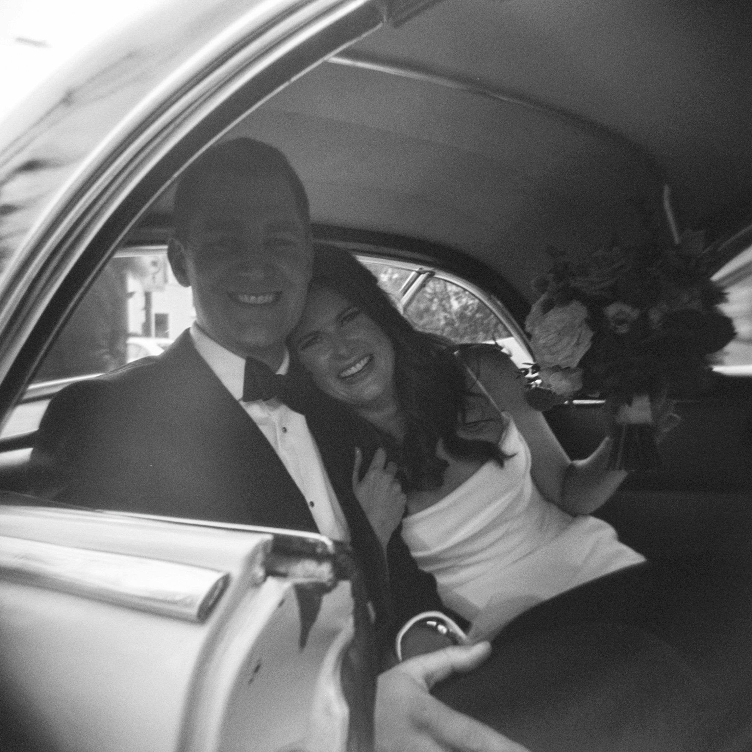 Black and white film photo of bride and groom in vintage car