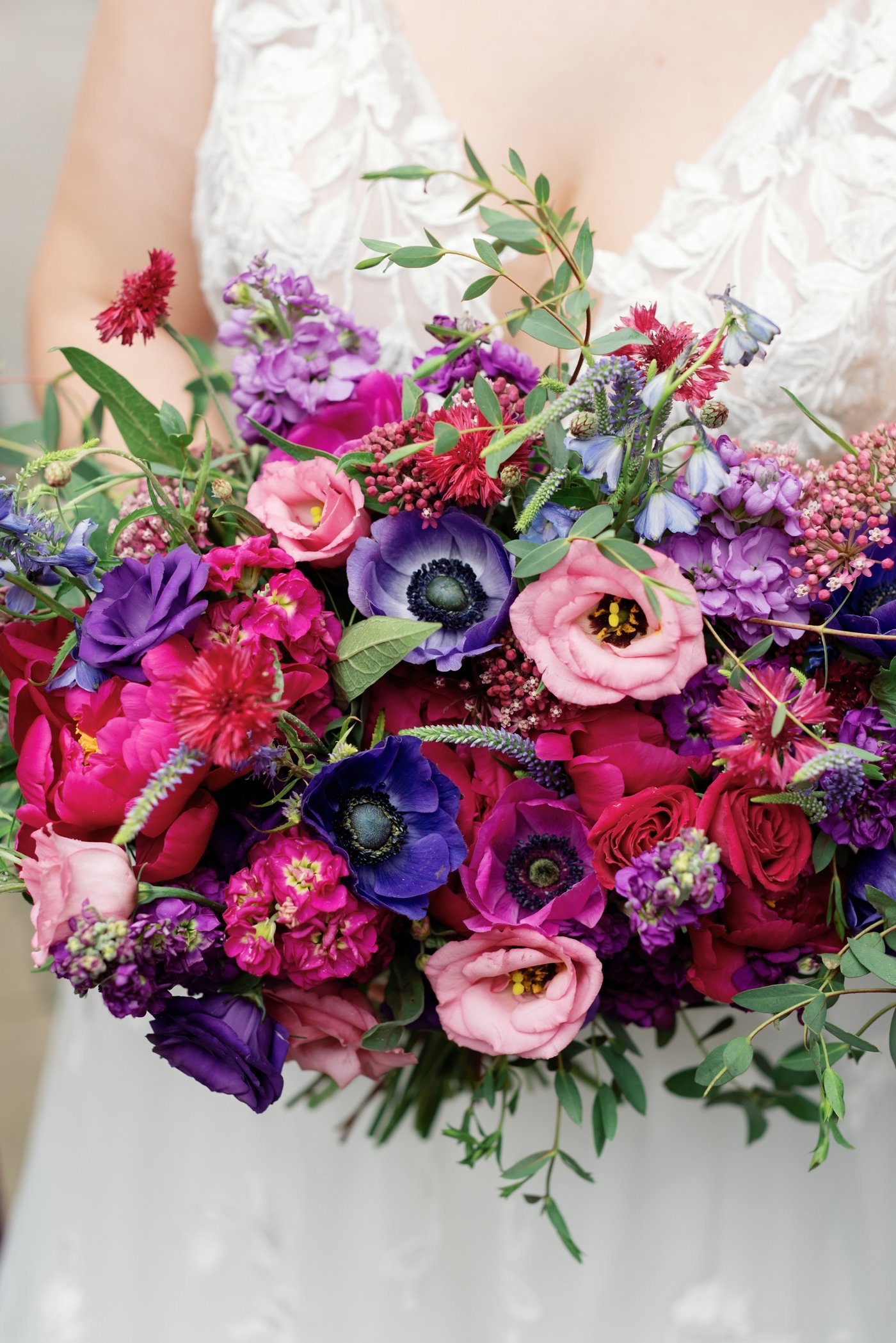 Purple and pink bridal bouquet filled with anemones, roses, and delphinium