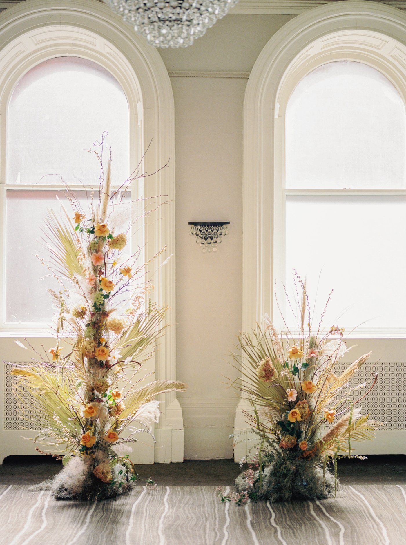 Broken arch wedding ceremony backdrop with peach roses, pampas grass, and dried palm leaves