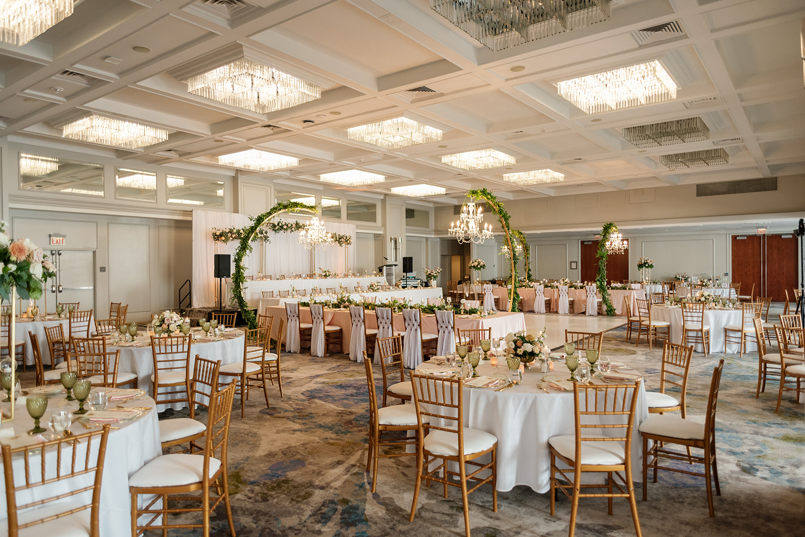 Spacious ballroom at The Westin Nova Scotian with round tables, gold chairs, floral centerpieces, greenery arches, chandeliers, and soft elegant décor set for a formal wedding reception.